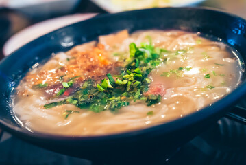 Close up - Vietnamese noodles in a black bowl topped with chopped spring onions.