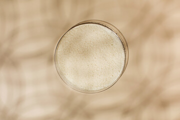 Hydrolyzed collagen powder in a Petri dish on a beige background with a shadow. 