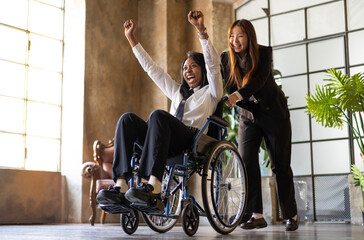 Young asian woman pushing  african american collegue in wheelchair in co-working studio-  Good...