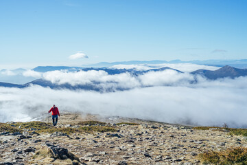 Solitaire hiker with walking stick climbing up  mountainous landscape with clouds gripping to the...