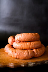 Sausages on a black background. Sausages on a wooden plate. Natural tasty sausages for children and adults.