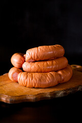 Sausages on a black background. Sausages on a wooden plate. Natural tasty sausages for children and adults.