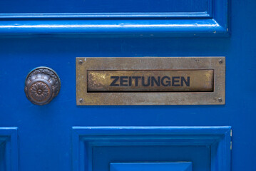 Close-up of blue wooden door with mail slot and text Zeitungen (German, translation is newspapers) on a cloudy summer day. Photo taken June 28th, 2022, Zurich, Switzerland.