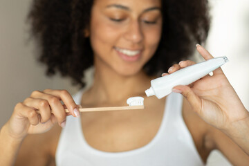 Female hands are pouring toothpaste on a toothbrush and a blurred face of a girl in the background.