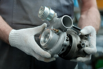 Car maintenance. An auto mechanic holds a new turbocharger in his hands. Inspection and control of the spare part for the engine for compliance and integrity.
