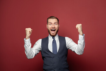 Happy excited businessman portrait. Guy winning, achieve prize or goal, have great news, fist pump and smiling on red banner background