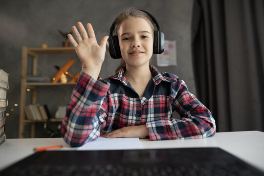 Student girl having video lesson using laptop in living room, studying with laptop computer. Distance Learning. enjoying online education, waving hand, webcam view