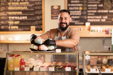 male coffee shop owner near showcase with cakes and desserts in his cafe, work in the cafeteria