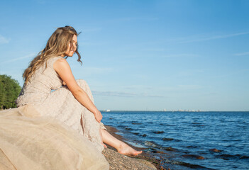 Fototapeta na wymiar Young cute barefoot girl model in a beige dress on the beach