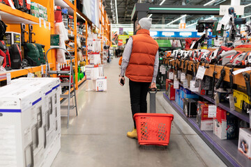 a buyer in a construction hypermarket walks between the rows with a basket on wheels