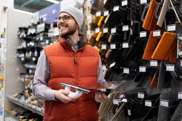 a buyer in a construction hypermarket next to a rack with paper wallpaper cannot decide on a choice