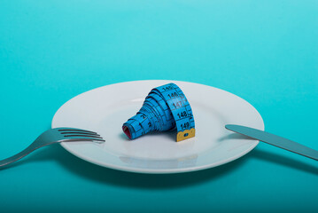 Healthy food, fitness for weight loss. An empty plate with a forkknife measuring tape in centimeters on a blue background from above. Diet menu Obesity. Place for an inscription. Advertising. - 514610604