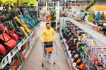 lawn mower shop customer walks between rows of battery electric petrol lawn mowers