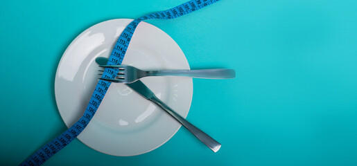 Healthy eating, weight loss obesity. An empty plate with a measuring tape in centimeters, a fork and a knife on a blue background from above. Diet menu.Place for an inscription. Advertising. - 514610632