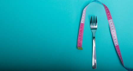 Healthy eating, weight loss obesity. Fork cutlery with a measuring tape in centimeters on a blue background from above. Diet menu.Place for an inscription. Advertising. - 514610688