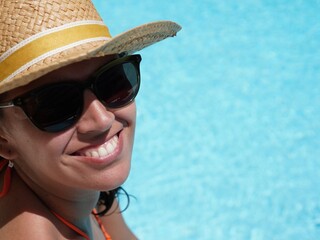 Profile view of tanned caucasian woman sunbathing by the pool with straw hat smiling for being relaxed on vacation in europe, concept relaxed lifestyle on vacation