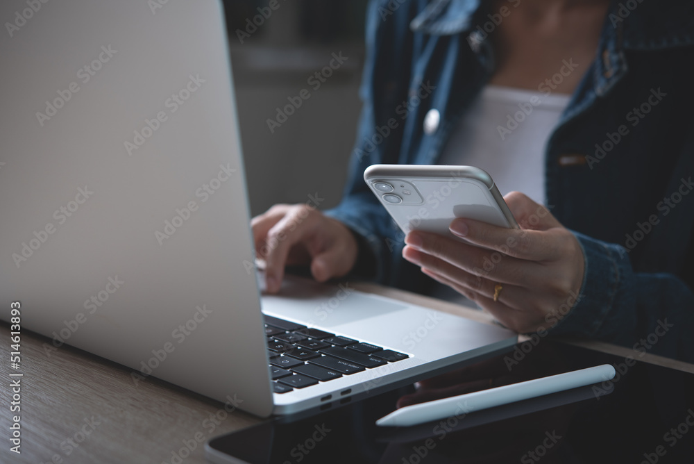 Poster closeup of business woman using mobile smart phone and working on laptop computer with digital table