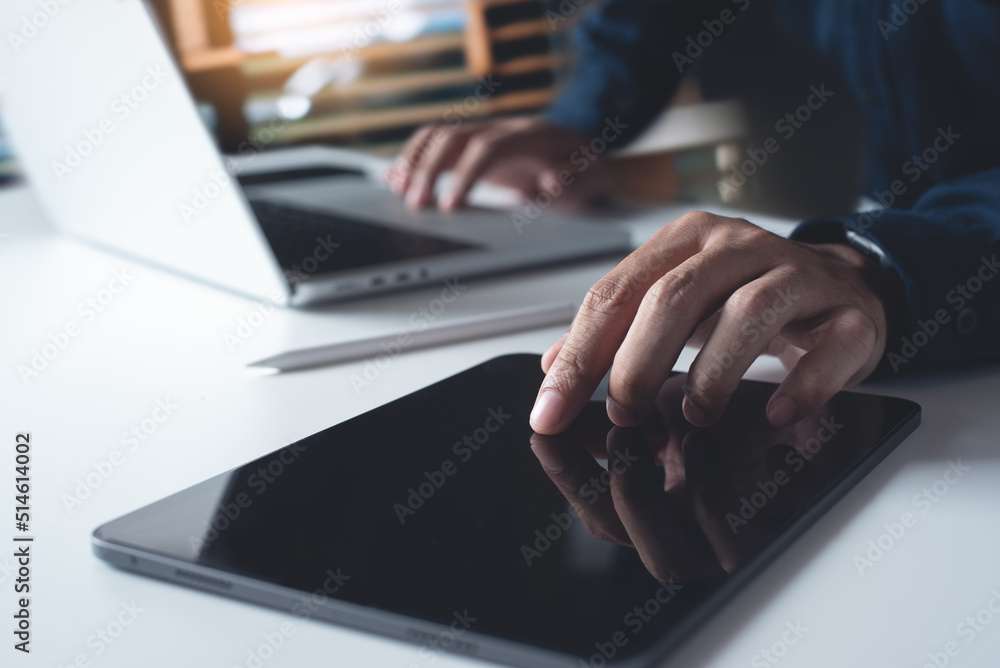 Wall mural Man using digital tablet, working on laptop computer on office table. Casual business man touching on tablet screen, surfing the internet, online job, freelance at work, close up