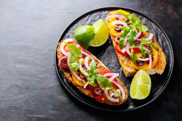 Vegetarian sandwiches on a dark background. Spanish tapas with vegetables, greens, olives and lime. Healthy sandwiches on a black plate. Top view. Copy space
