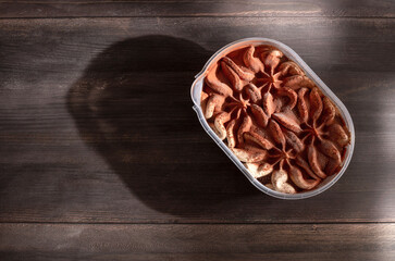 plastic container with ice cream tiramisu isolated on wooden background