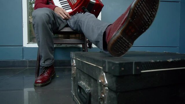 A well-dressed man is sitting on a chair and playing a red accordion traditional musical instrument on the terrace of the house