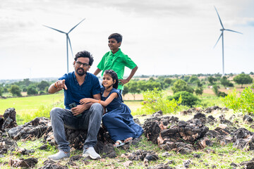 Happy smiling father with kids on top of mountain near wind power fans having good time - concept...