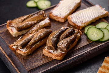 Delicious fresh sandwich with sprats with crispy toast, butter and cucumber - obrazy, fototapety, plakaty