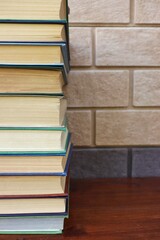A stack of books lies on a wooden table against a brick wall