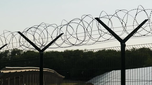 Razor wire fence around the solar power plant during sunset. Mesh Fence. Fencing the territory on which the solar power elements. Field of solar panels behind barbed wire.
