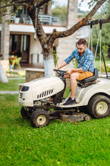 Gardener driving a riding lawn mower in a garden.