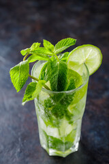 Mojito cocktail on a dark background. Summer cocktail with lime, mint and ice cubes. Refreshing citrus drink