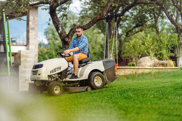Fototapeta na wymiar Portrait of gardener using a lawn mowing tractor for cutting grass. professional gardening details