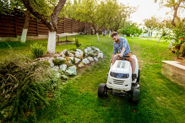 Man cutting grass in his garden yard with lawn mower, landscaping works. Professional gardener driving a tractor.
