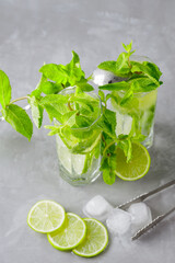 Mojito cocktail on a gray background. Two glasses of cocktail with mint, lime and ice. Bar tools and ingredients for cocktail