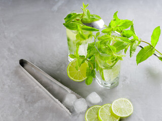 Mojito cocktail on a gray background. Two glasses of cocktail with mint, lime and ice. Bar tools and ingredients for cocktail