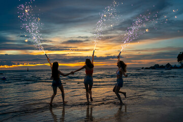 Young Asian woman having fun dancing and playing sparklers together on tropical island beach in summer night. Happy female friends enjoy outdoor lifestyle nightlife on holiday travel vacation trip