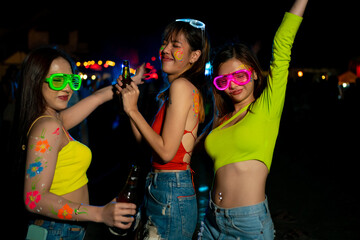 Group of Asian woman having fun celebrating and dancing together at full moon night party at koh phangan beach in Thailand. Happy female friends enjoy outdoor activity lifestyle on summer vacation