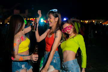 Group of Asian woman having fun celebrating and dancing together at full moon night party at koh phangan beach in Thailand. Happy female friends enjoy outdoor activity lifestyle on summer vacation