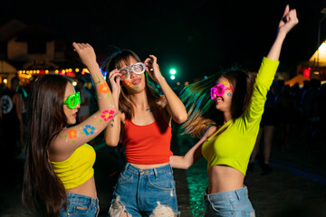 Group of Asian woman having fun celebrating and dancing together at full moon night party at koh phangan beach in Thailand. Happy female friends enjoy outdoor activity lifestyle on summer vacation