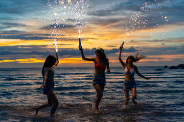 Young Asian woman having fun dancing and playing sparklers together on tropical island beach in...