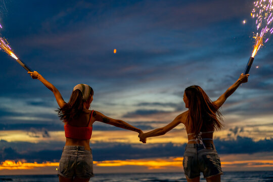 Young Asian Woman Having Fun Dancing And Playing Sparklers Together On Tropical Island Beach In Summer Night. Happy Female Friends Enjoy Outdoor Lifestyle Nightlife On Holiday Travel Vacation Trip