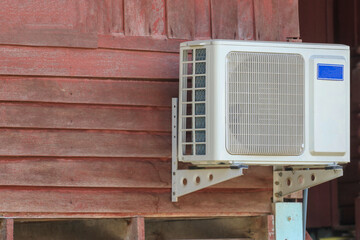 The air conditioner condenser is mounted on the wall of a wooden house.