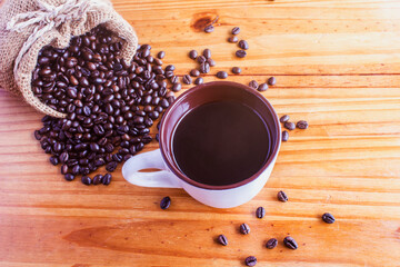 A cup of black coffee and a bag of coffee beans on an old wooden floor.