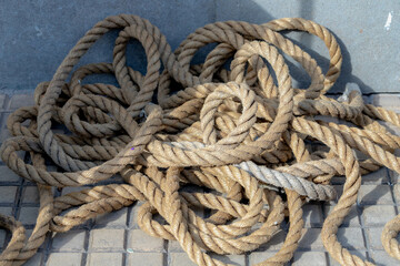 Stacked and massey of old rope on the concrete floor, A rope is a group of yarns, plies, fibers or...