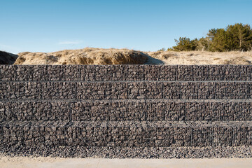 Gabion wall of metal mesh cage filled with rocks protects sand dunes