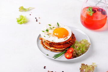 Fried egg on the stack of zucchini fritters and berry lemonade in the glass on white table. Served lunch on the plate
