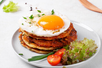 Fried egg on the stack of zucchini fritters with fresh vegetables. Served breakfast on the plate