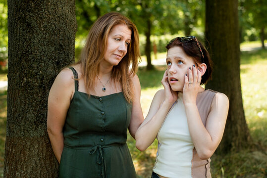 Mother and daughter are talking in the park, mother lovingly looks at teenage daughter and says something to her, and the daughter covers her ears and defiantly turns away from mother