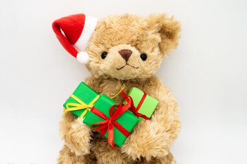 A stuffed toy Teddy bear in a red Santa Claus hat with a pompom on one ear, holding green gift boxes in its paws. White background, copy space. The concept of Christmas gifts, sales