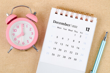 December 2022 Desk calendar with pink alarm clock on brown background.